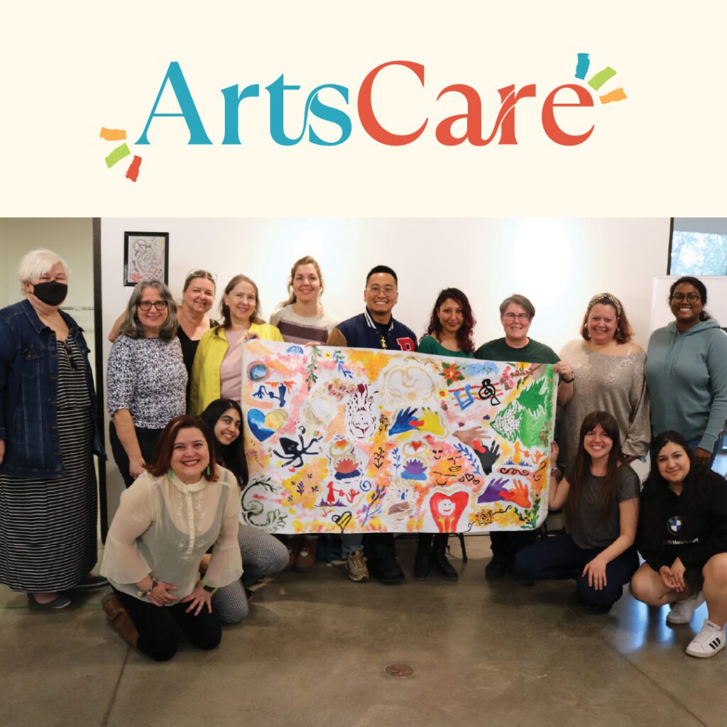 A group of people pose together indoors, holding a colourful collaborative artwork featuring various artistic elements like hearts, hands, and abstract designs. The "ArtsCare" logo is displayed at the top.