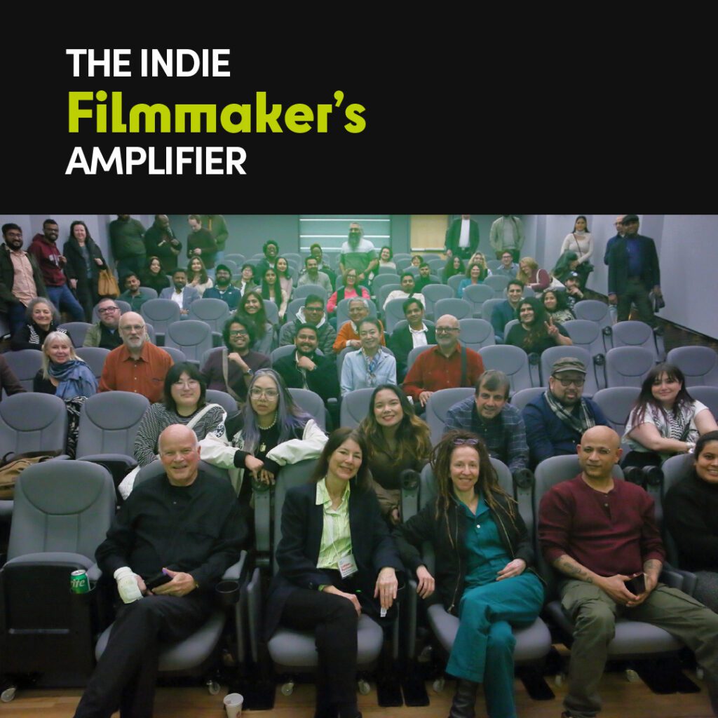 A large group of attendees is seated in a lecture hall, smiling at the camera. The event title, "The Indie Filmmaker’s Amplifier," is displayed at the top in bold white and green text.